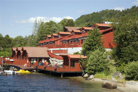 LUX-leilighetene på Mones Feriesenter — store røde bygg med solrike terrasser ned mot vannkanten.